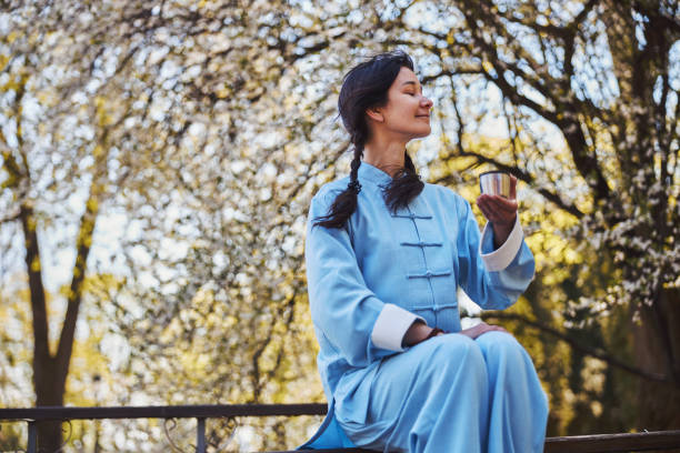 Satisfied martial artist having a break with tea in nature Asian female dressed in blue martial arts uniform turning her face to side and enjoying the wind while holding tea kungfu tea stock pictures, royalty-free photos & images